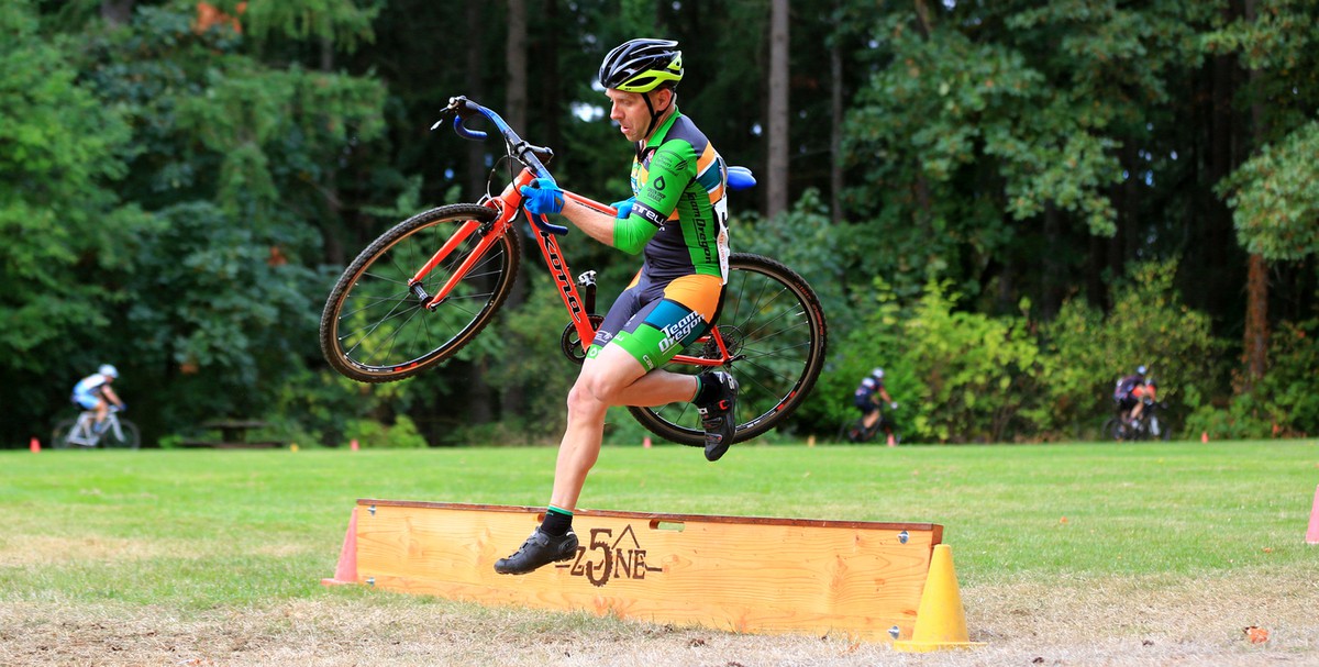 Man in cyclocross skinsuit jumping a barrier with a bicycle at a race