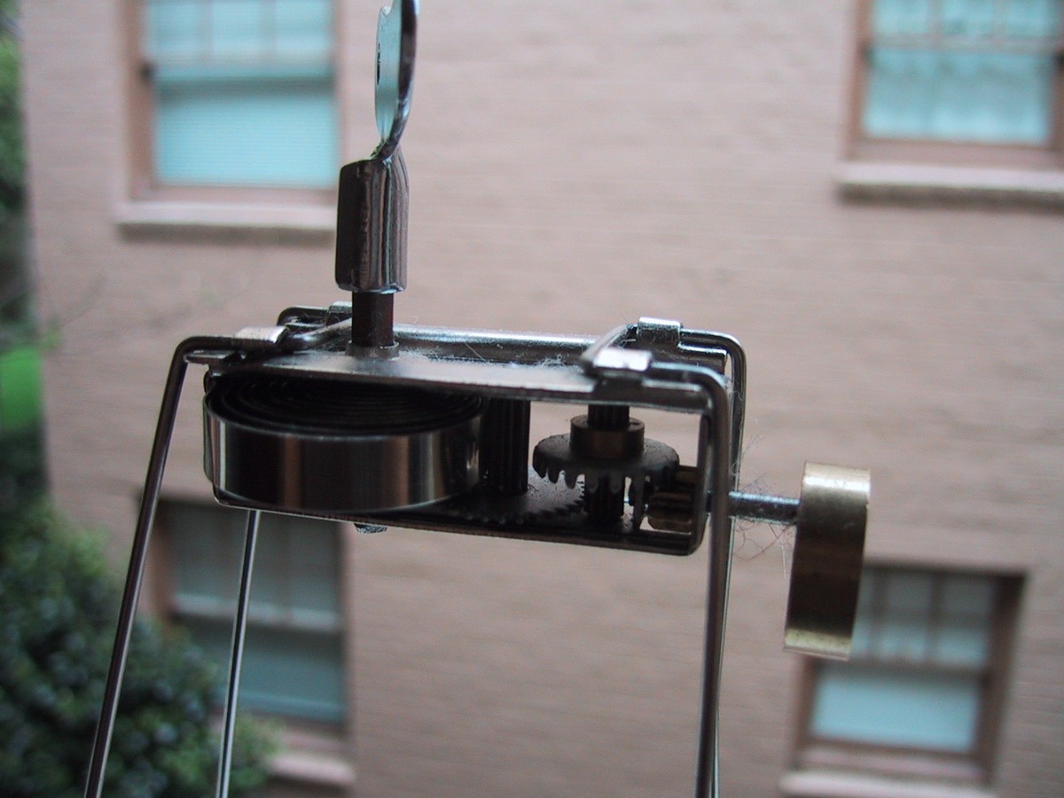 Closeup of a spindly windup toy of uncertain purpose, on a windowsill looking into the courtyard of an apartment building