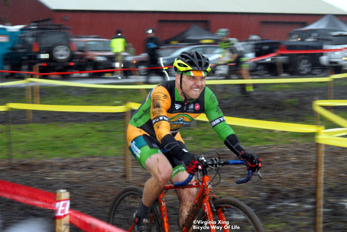 middle aged man racing in cyclocross skinsuit, biting his lower lip, covered in mud, in the driving rain, motion blur. Credit: ©Virginia Xing, Bicycle Way of Life