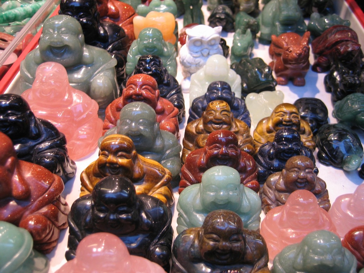 Closeup of several small Buddha figurines (and one owl, and one rabbit) carved in various minerals like jade and soapstone, for sale in a Hong Kong street market