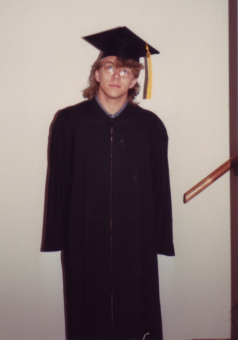 Indoors, teenage boy with mullet, wearing graduation gown and mortarboard