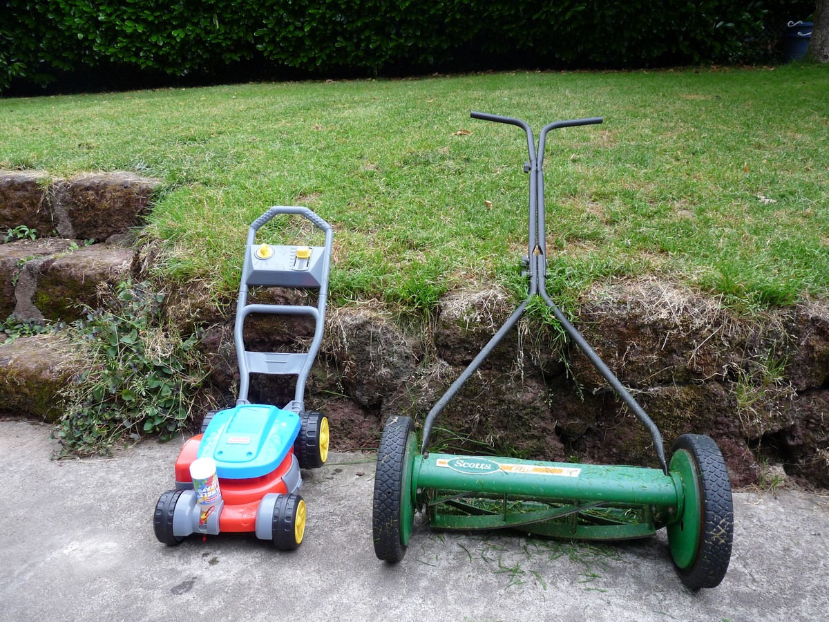 Plastic toy lawnmower and a reel or “push” mower, side by side