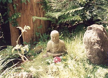 Closeup of a small stone buddha with a flower in front of it, taken at the San Francisco Japanese Gardens, 1992