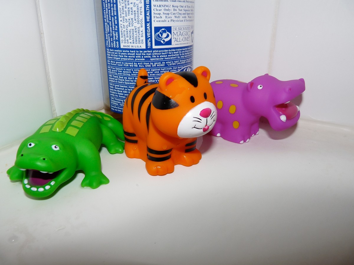 Closeup of three animal squirty bath toys and a bottle of Dr. Bronner’s soap, on the ledge of a bathtub
