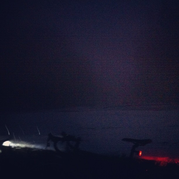 Extremely dark photo taken at Council Crest park in the snow, late at night. The headlight and tail light of a bicycle are visible