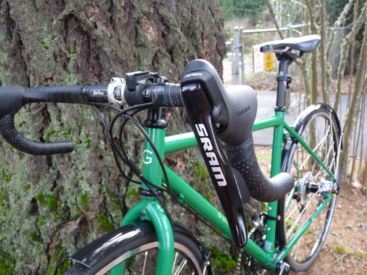 Closeup of the handlebars and top tube of a bright green cyclocross style bicycle, with the left shifter pod branded “SRAM” prominent in the frame