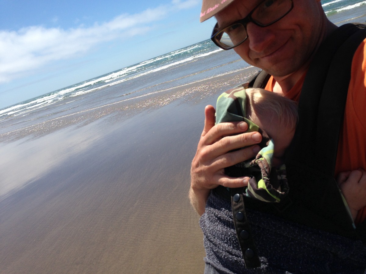 Selfie on a beach with Ada, asleep in the Ergo carrier
