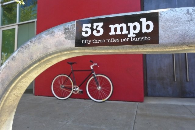 Sticker on a bike rack reading “53 miles per burrito”