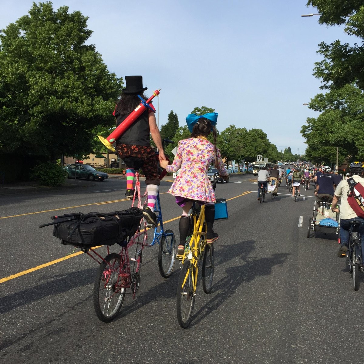 Olive Rootbeer and Dingo Dizmal on tall bikes, holding hands, shot from behind. Photo by @__P__J