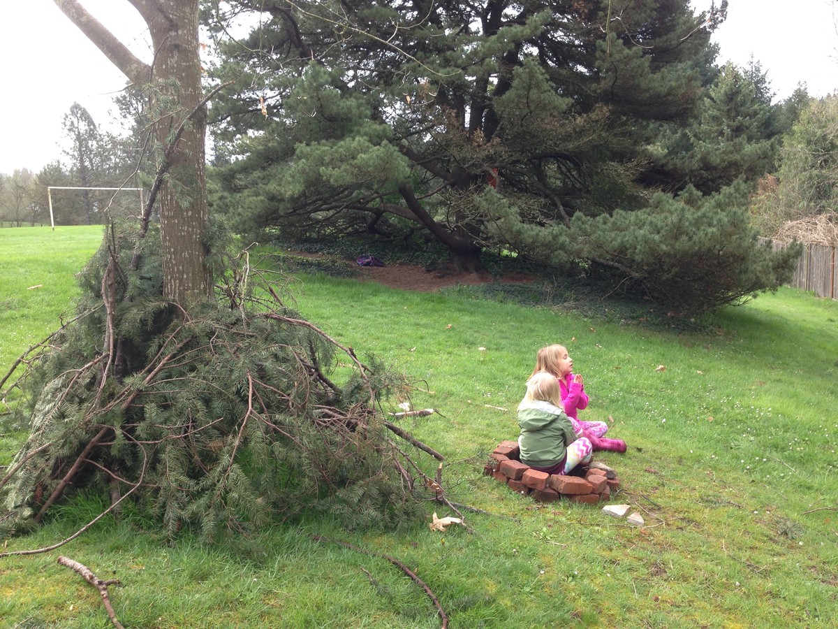 Two small children sitting in a circle of bricks in a park between two trees