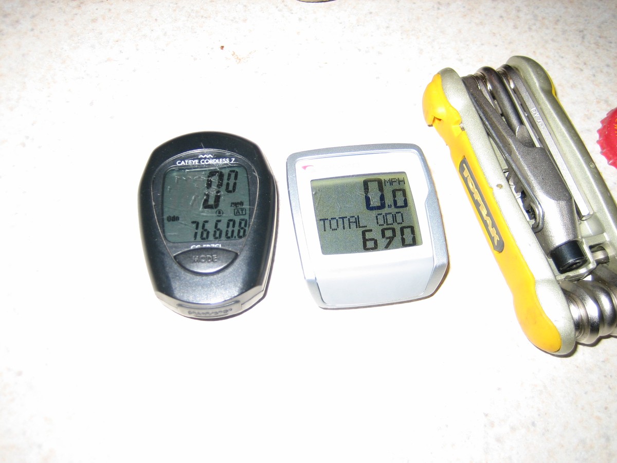 Close up of two digital bike computers reading 7660.8mi and 690mi. On the side of the frame is a bike multitool. All these things are grotty, chipped & beat up
