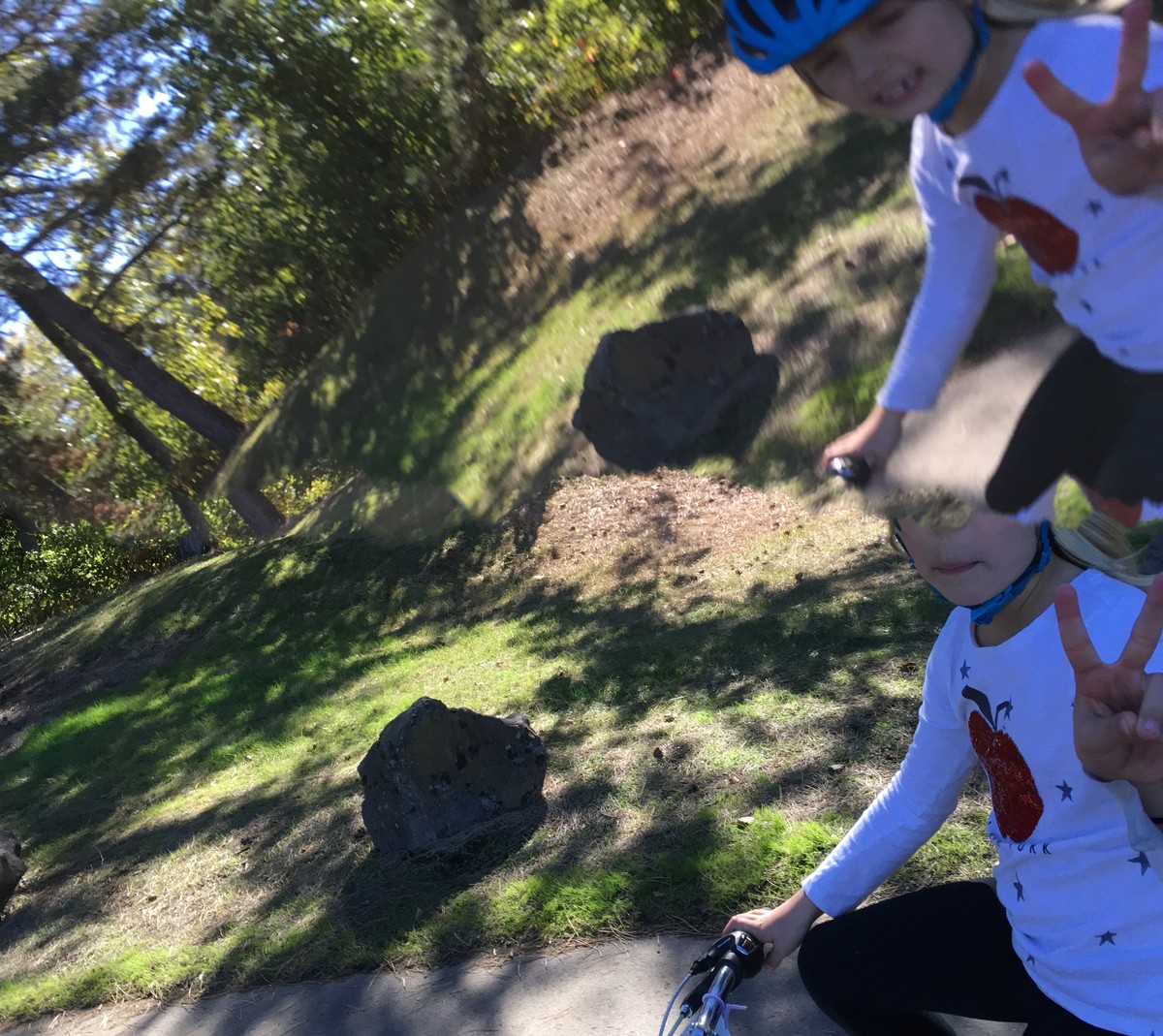 Digitally distorted photo of a young girl on a bicycle smiling and flashing the “V” sign. The Image is “bent” such that she appears twice, slightly superimposed over herself