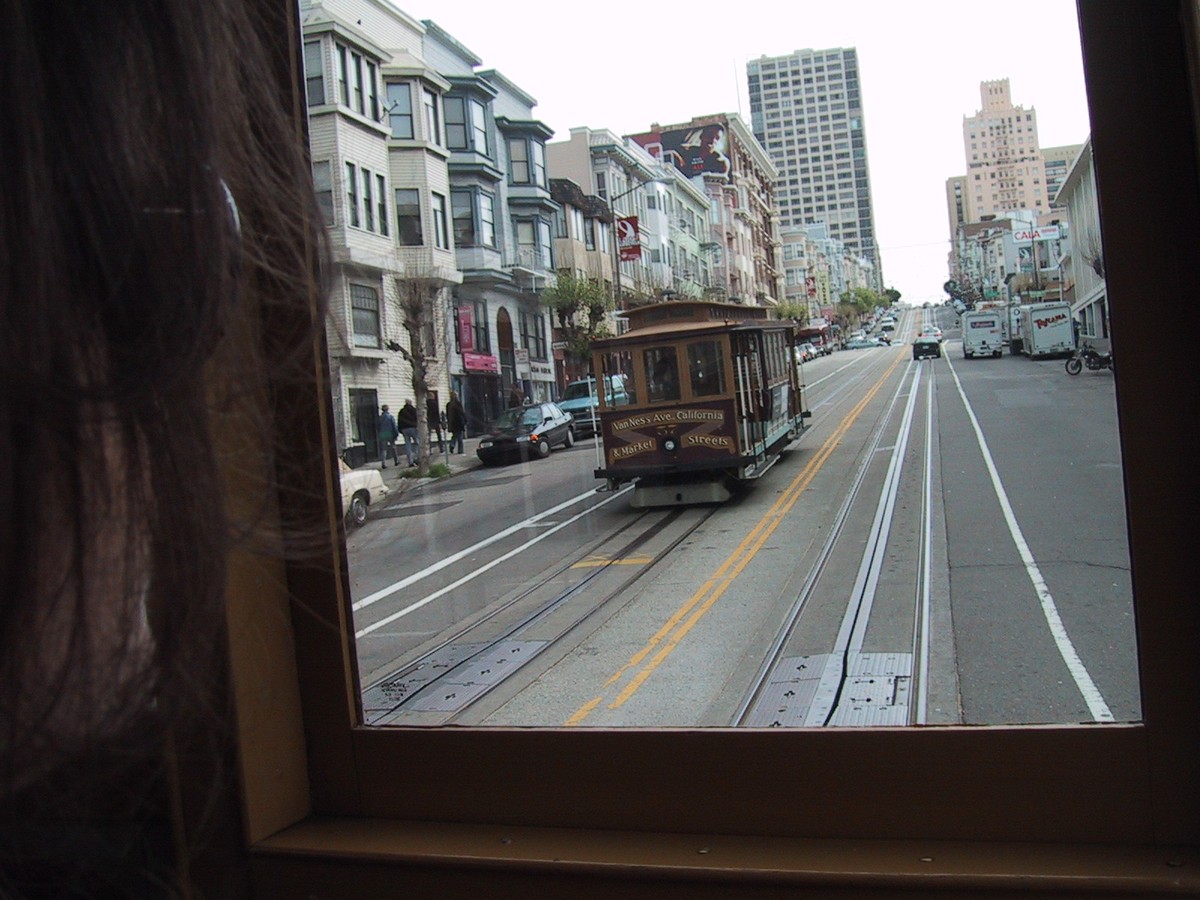 Shot out of the back of a cable car up a steep San Francisco Street; a woman’s face and hair is faintly visible in the near foreground looking out the window