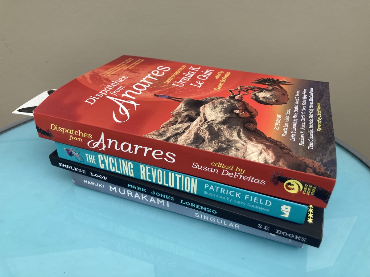 Four books in a pile: DISPATCHES FROM ANARRES,  CYCLING REVOLUTION by Patrick Field, ENDLESS LOOP by Mark Jones Lorenzo, and FIRST PERSON SINGULAR by Haruki Murakami