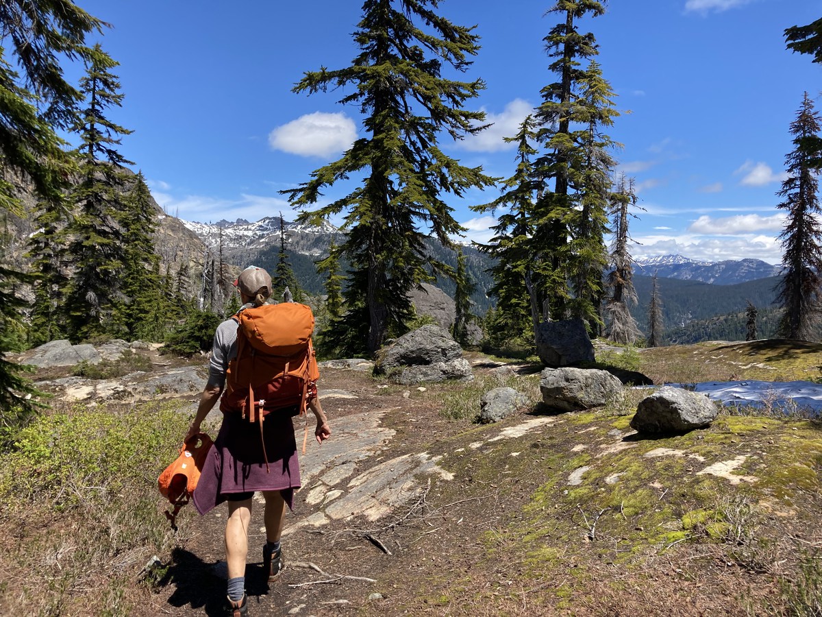 Somen wearing a backpack walking along a broad ridge with lightly glaciated peaks on the horizon