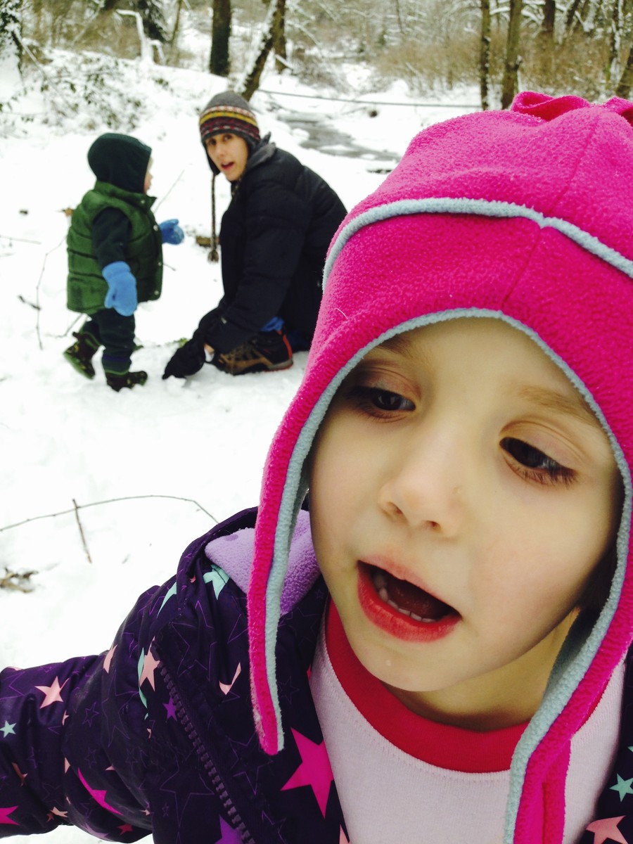 A woman, toddler, and preschooler playing in the snow. The preschooler is very close to the lens; the woman is crouching near the toddler about 10' distant