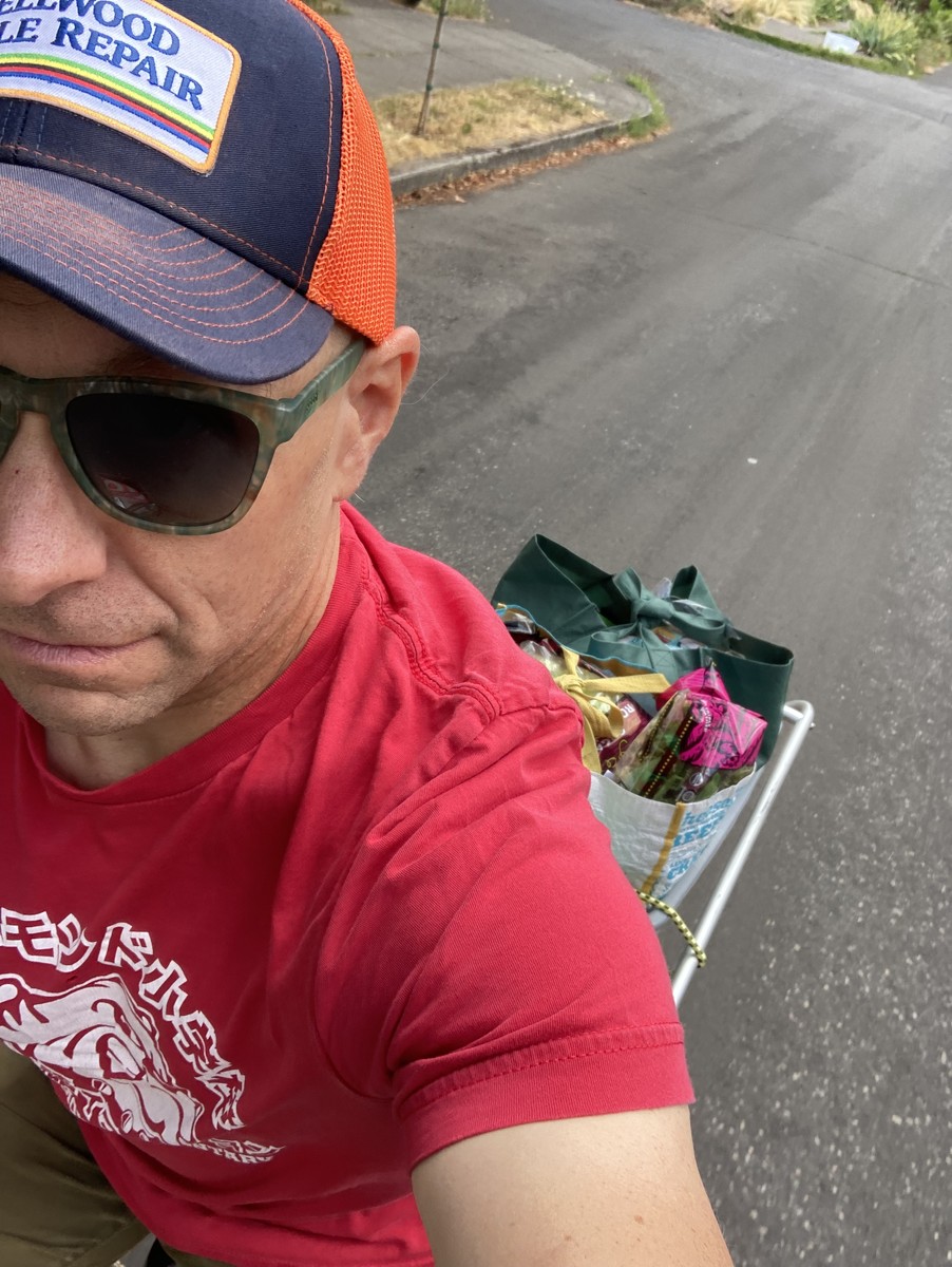 Selfie taken while riding the cargo bike, downward view, my face only partially visible, several bags of groceries on the bike behind me