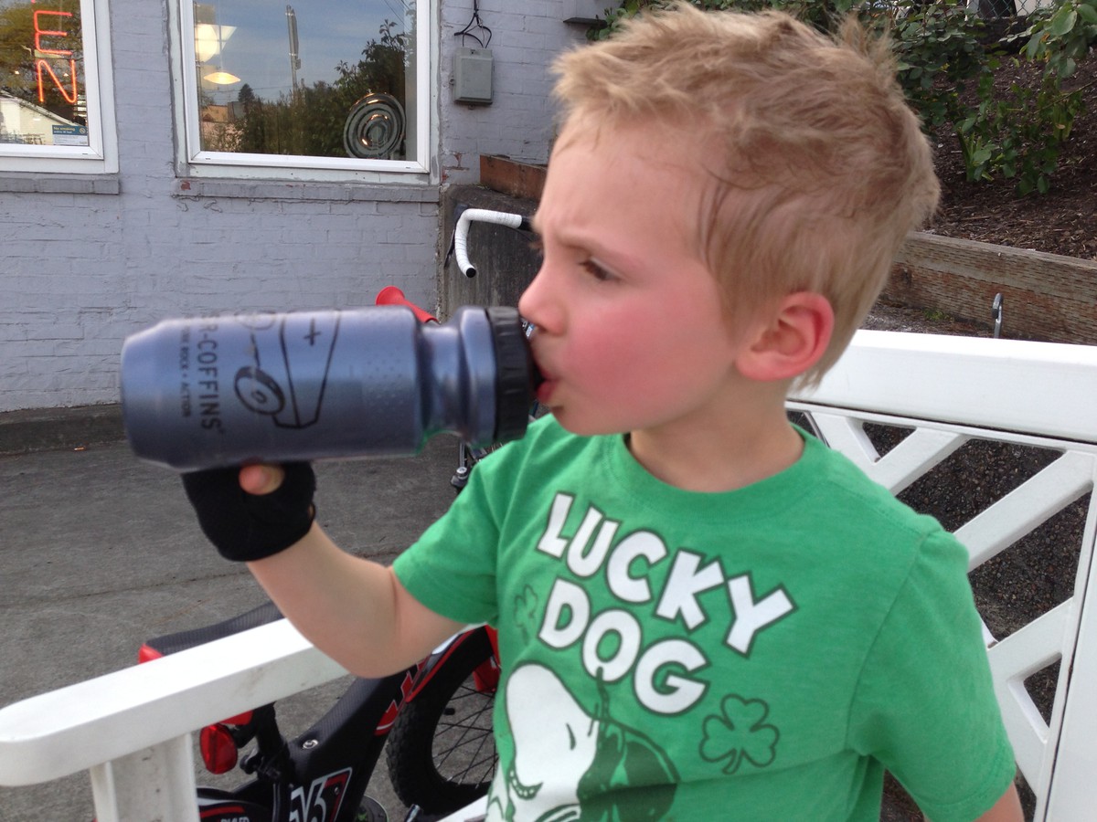 Sweaty young kid with bike gloves, in a Lucky Dog t-shirt, drinking from a bike bottle
