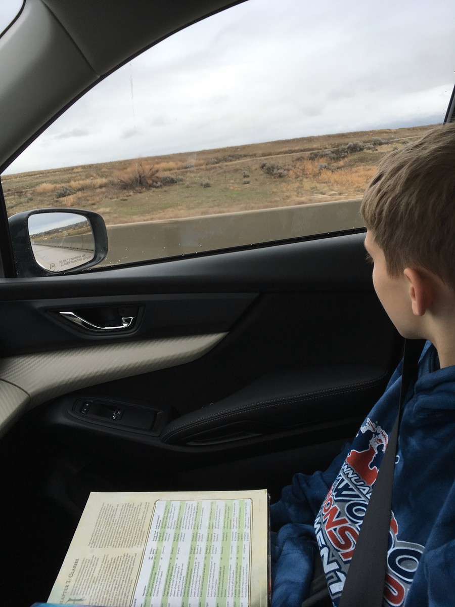School age boy with a book on his lap, looking out the window at a dry Idaho landscape