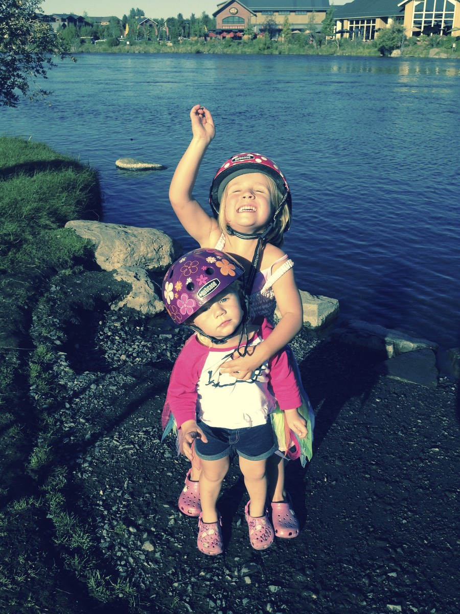 Toddler and preschooler in bicycle helmets standing next to a small river