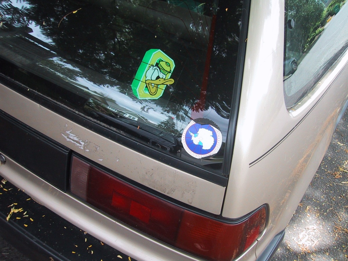Closeup of two decals on the right rear of a 1990 honda civic. One is an “Oregon duck” sticker; the other is of Antarctica