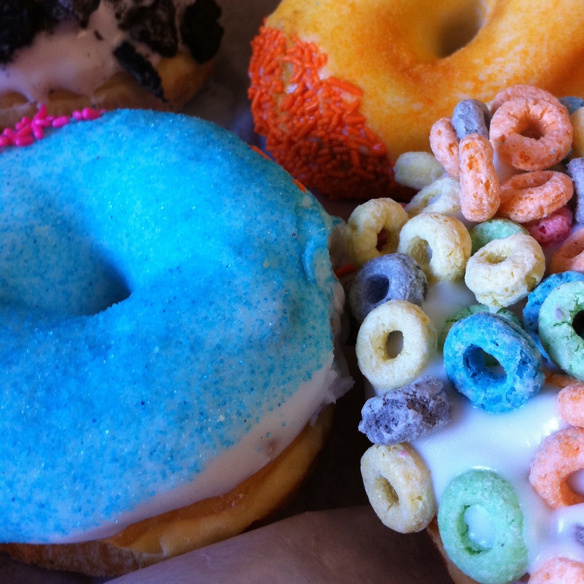 Closeup of brightly-frosted donuts. One donut has Froot Loops on it