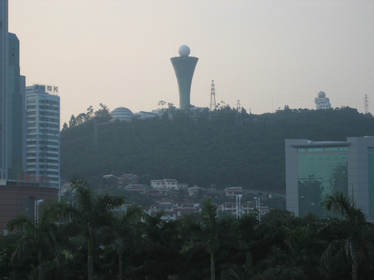Landscape taken at sunset of a tall, neomodern tower, on a forested hilltop above a Chinese city