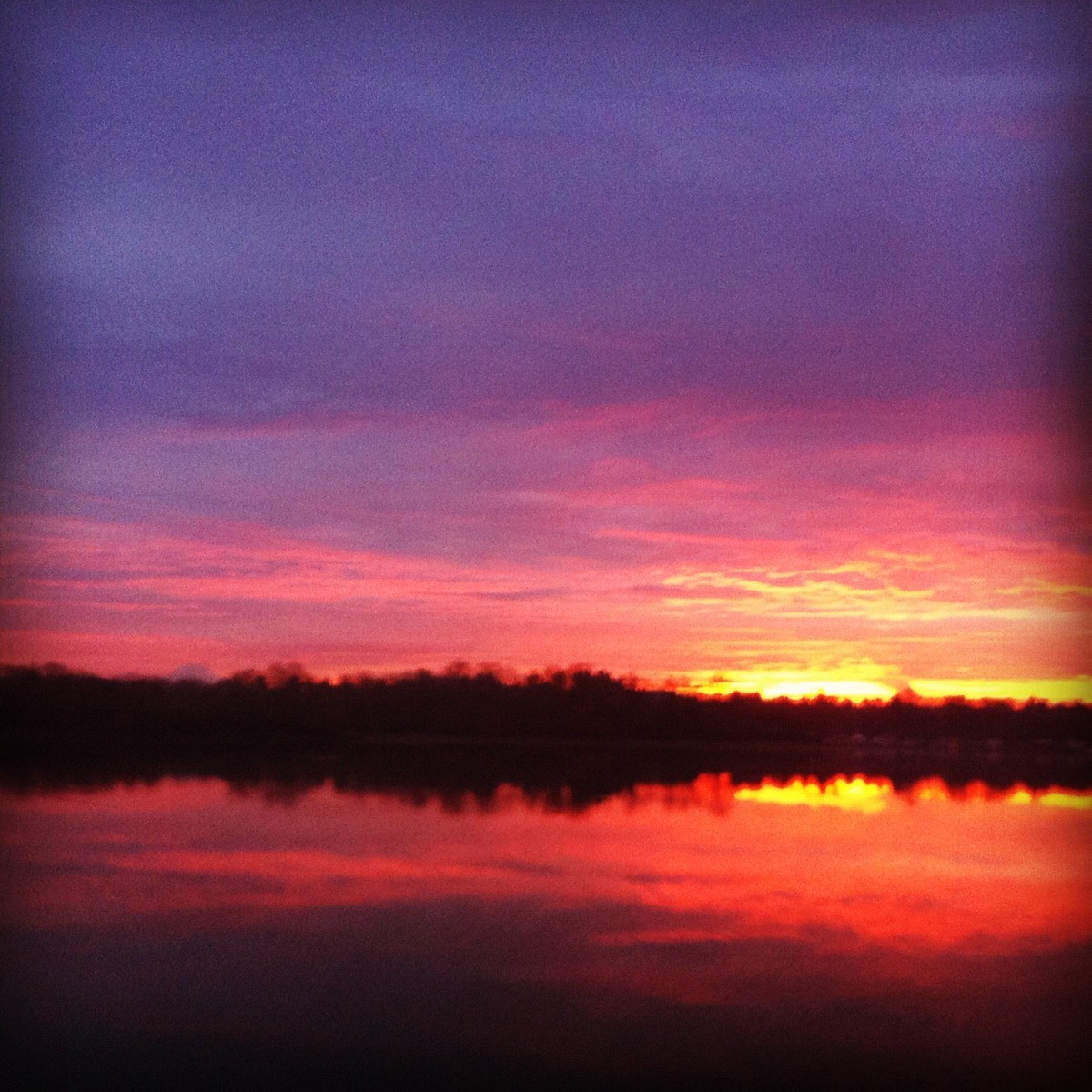 Heavily filtered riverscape, orange sky and rising sun reflected in the Willamette river
