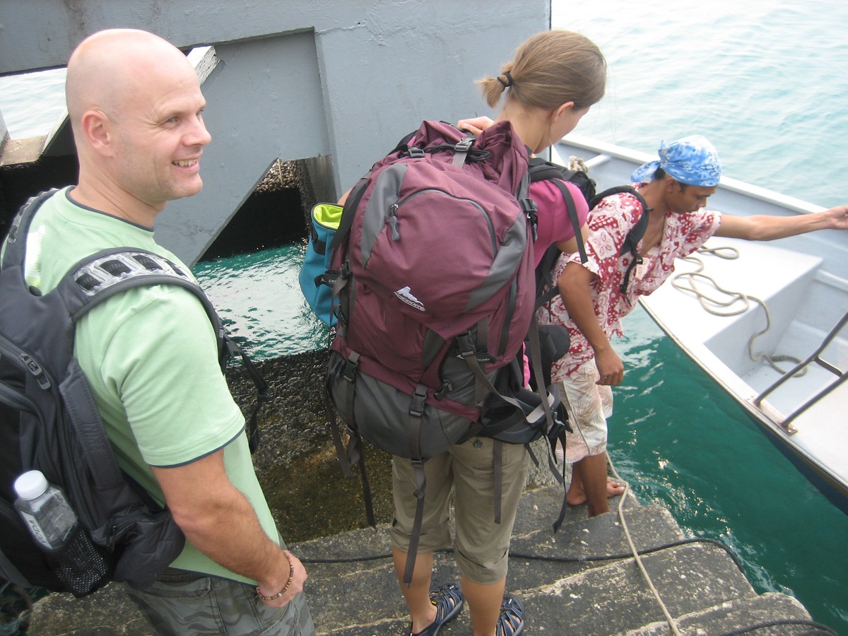 Two Western backpackers boarding a small boat captained by a lithe Malaysian man
