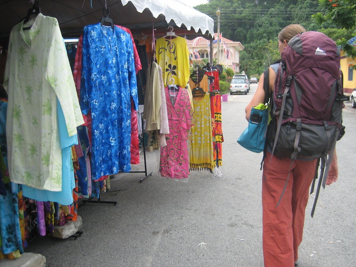 A female backpacker walking past an outdoor stall features coloful muumuus and sarongs