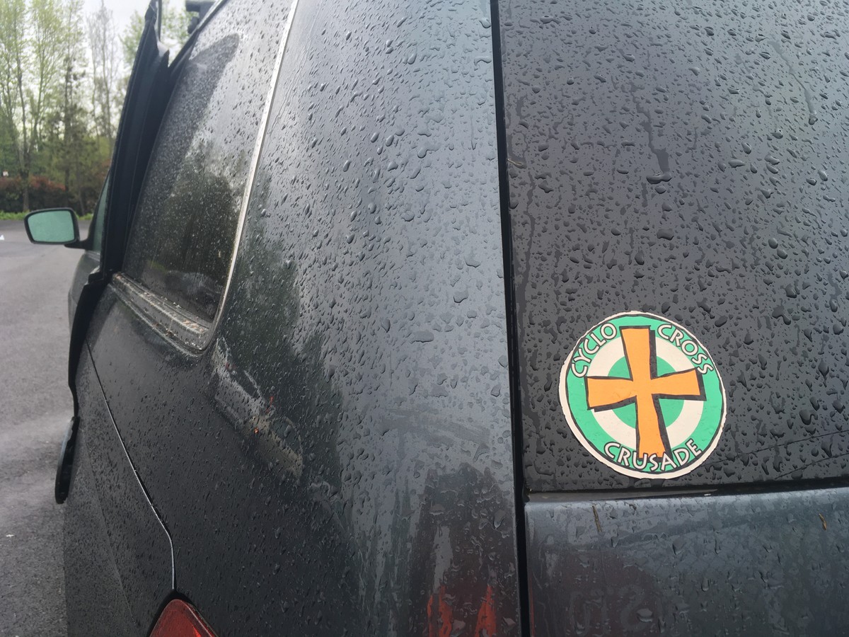 Closeup of a “Cyclocross Crusade” sticker on the window of a minivan, wet with rain