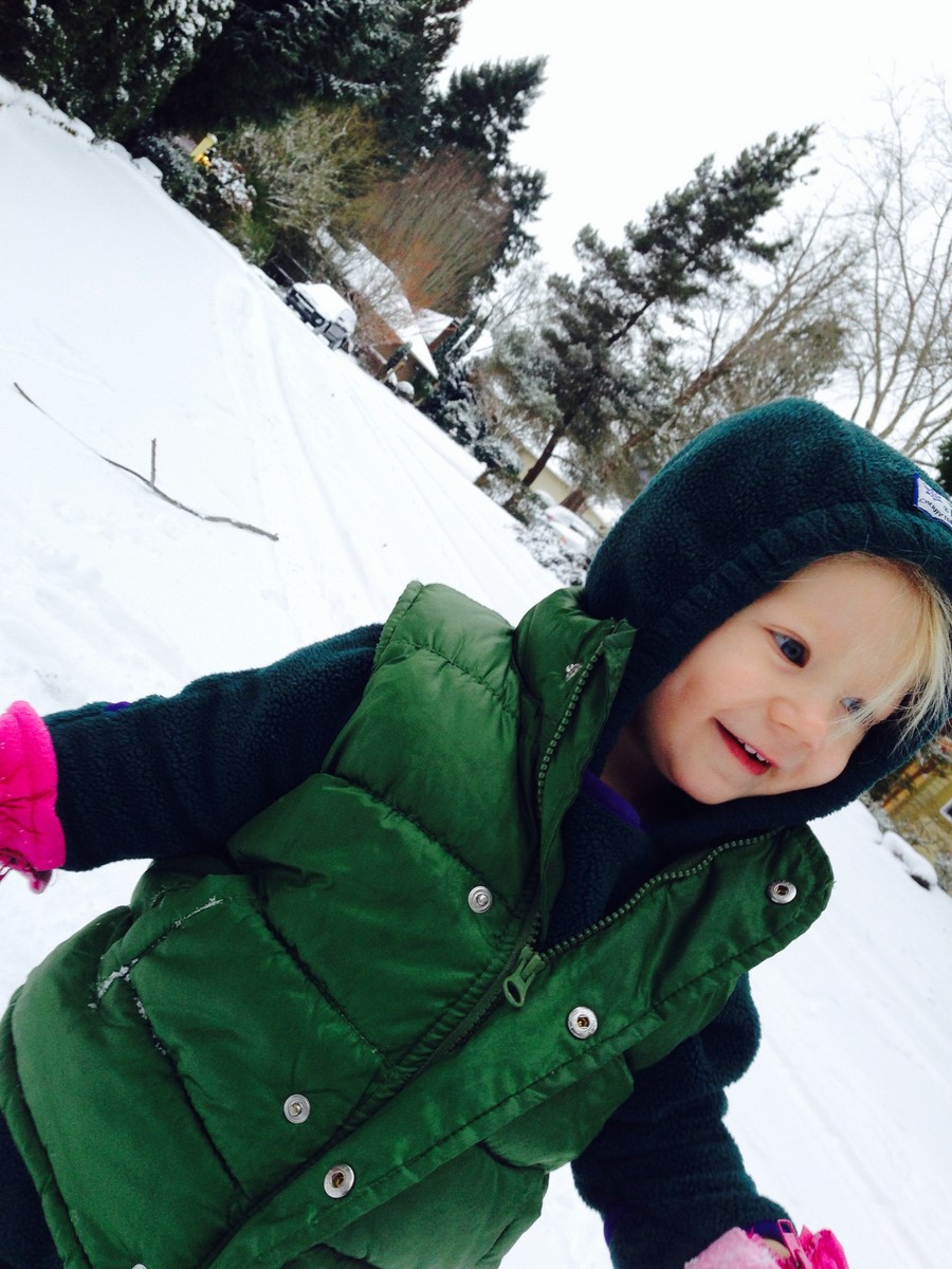 Toddler in hand-me-down snowclothes standing in the snow, smiling; Dutch angle