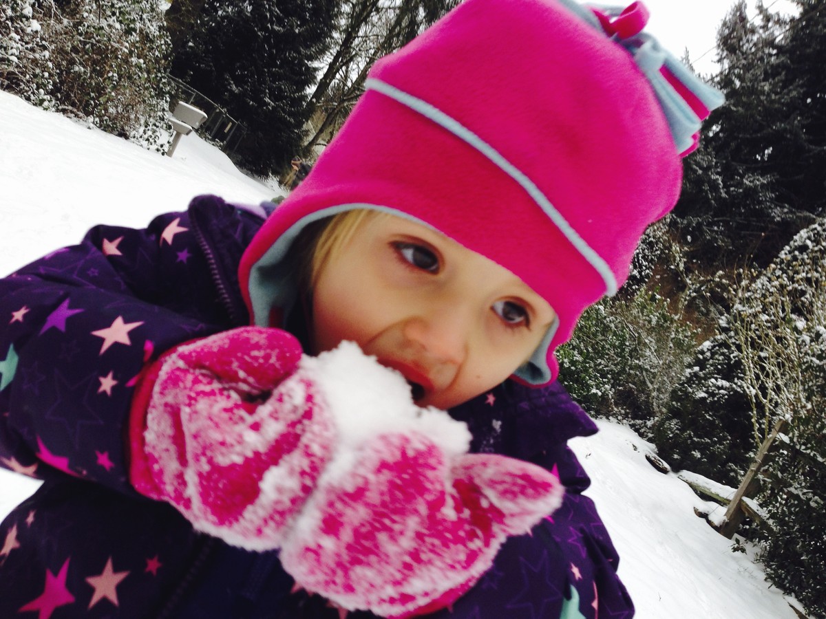 Preschool-age child in colorful snow clothes eating snow