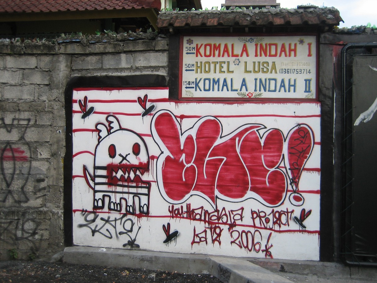 Graffiti on a wall with several signs for hotels; the wall is topped with broken glass