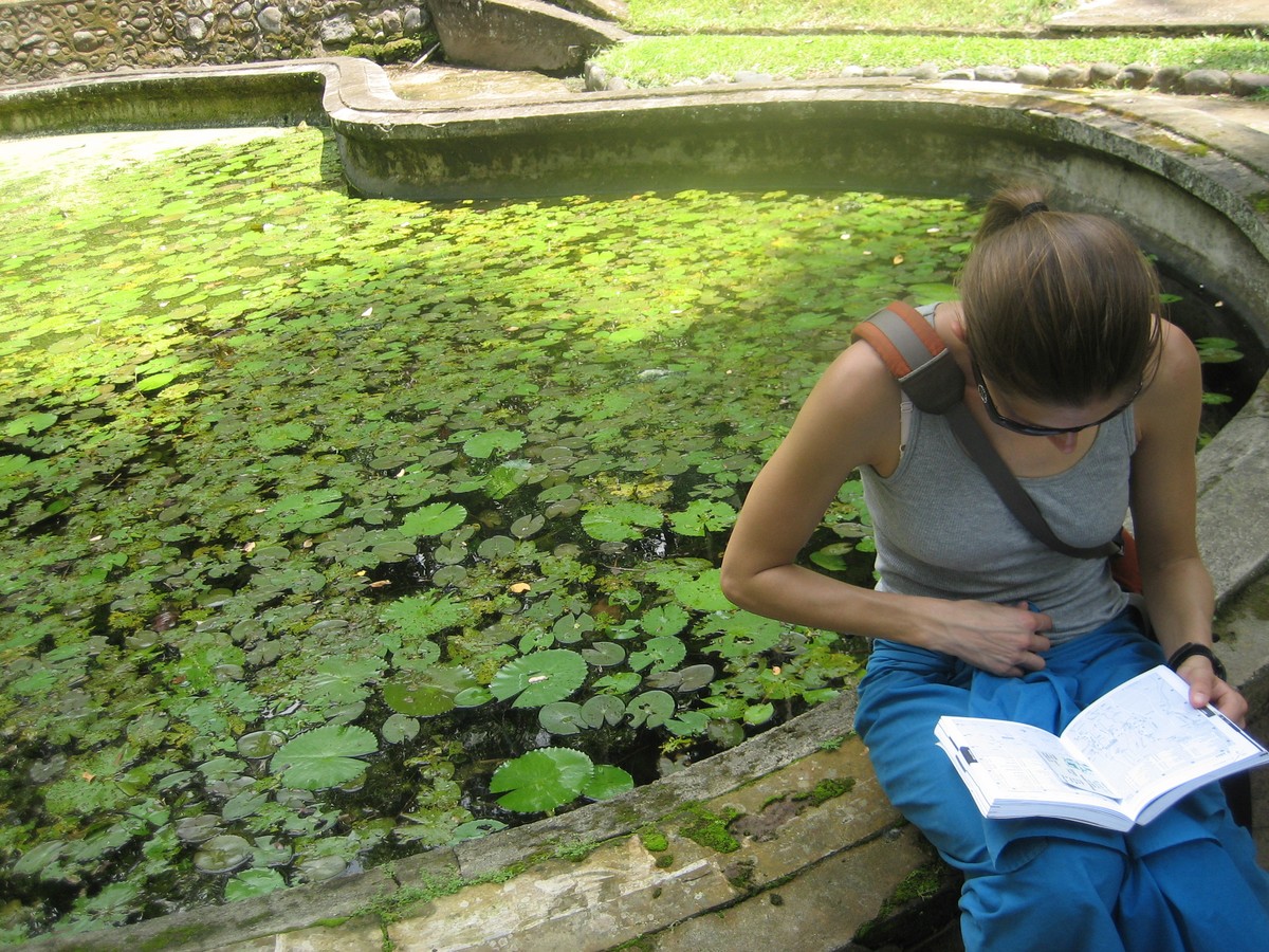 Jenny seated by a pond, reading the Lonely Planet Guidebook to Bali