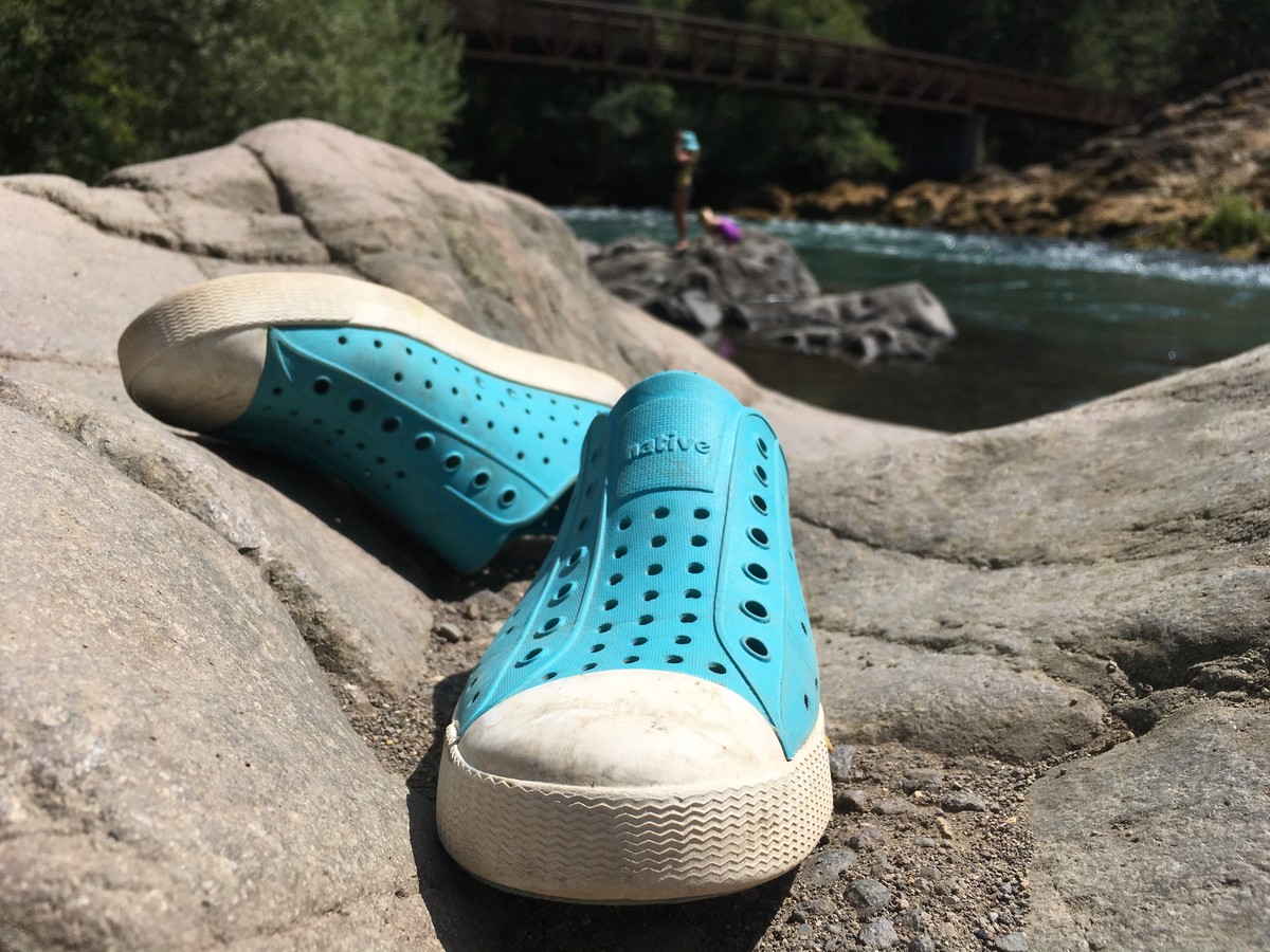 Closeup of a pair of kids’ water shoes on a rock at the side of a river