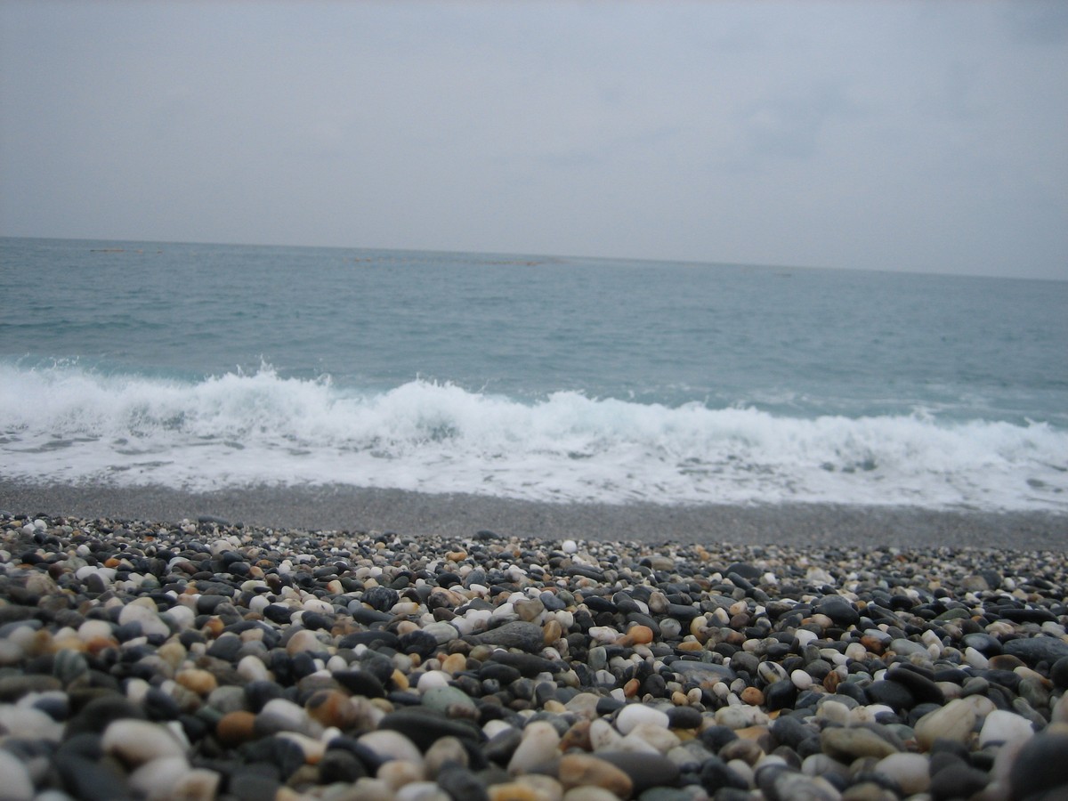 Low perspective shot of small waves lapping over a beach made of roughly dime-sized pebbles, most of which are well-rounded marble fragments