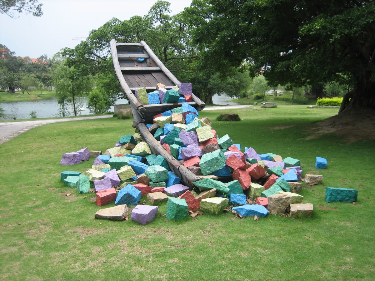Public artwork from Xiamen, Fujian: an old-style flatbottom boat on a grassy lawn, filled with blocks of stone painted bright colors; the boat appears to be capsizing and tipping these blocks onto the lawn