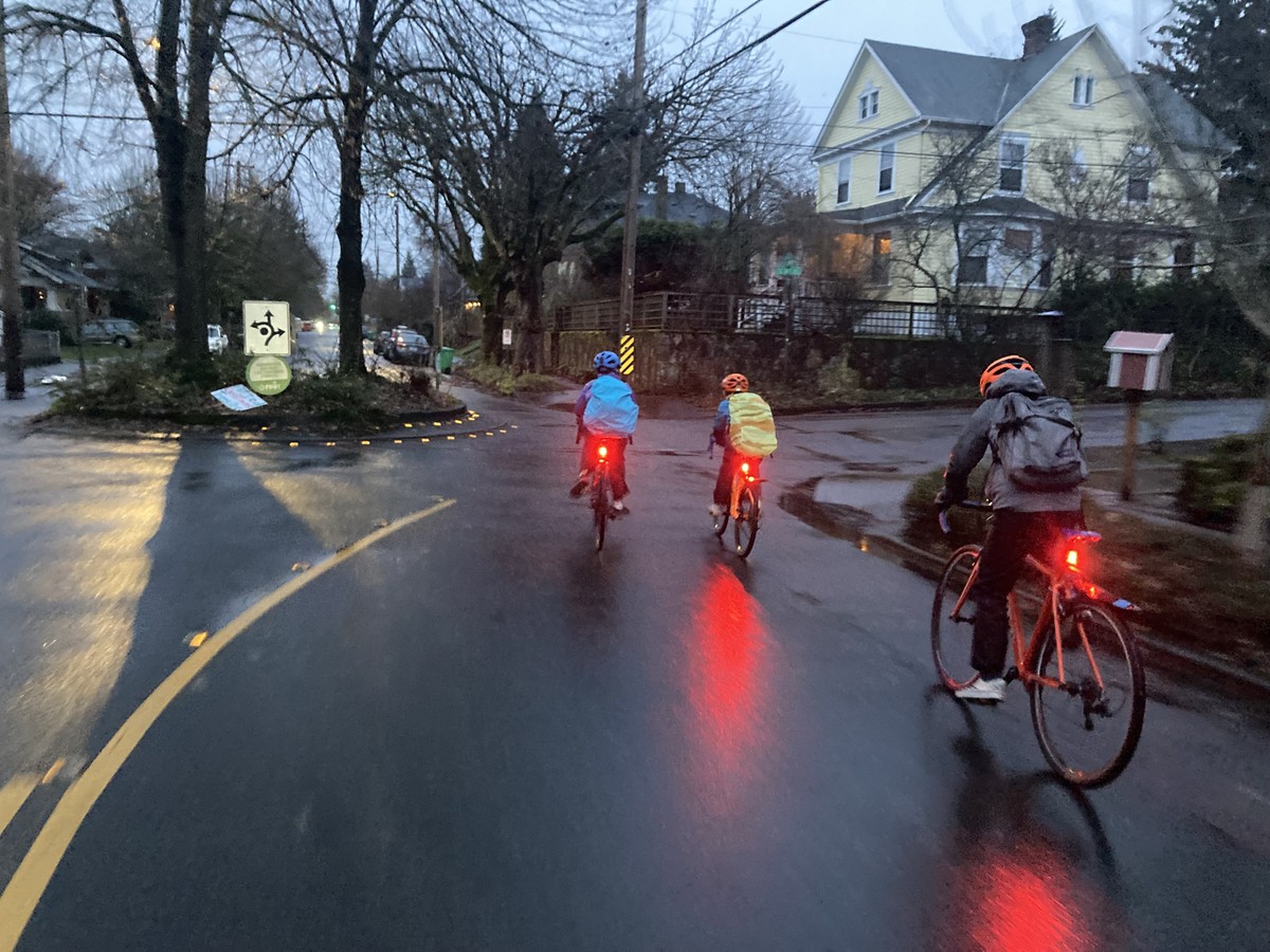 Three kids on bikes on a dark street, brightly illuminated with blinky lights and colorful gear