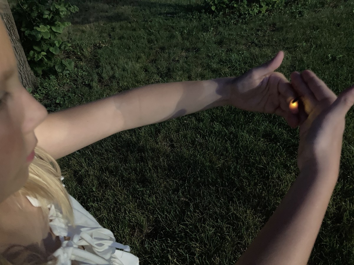 View from over the shoulder of a child gently holding a glowing firefly