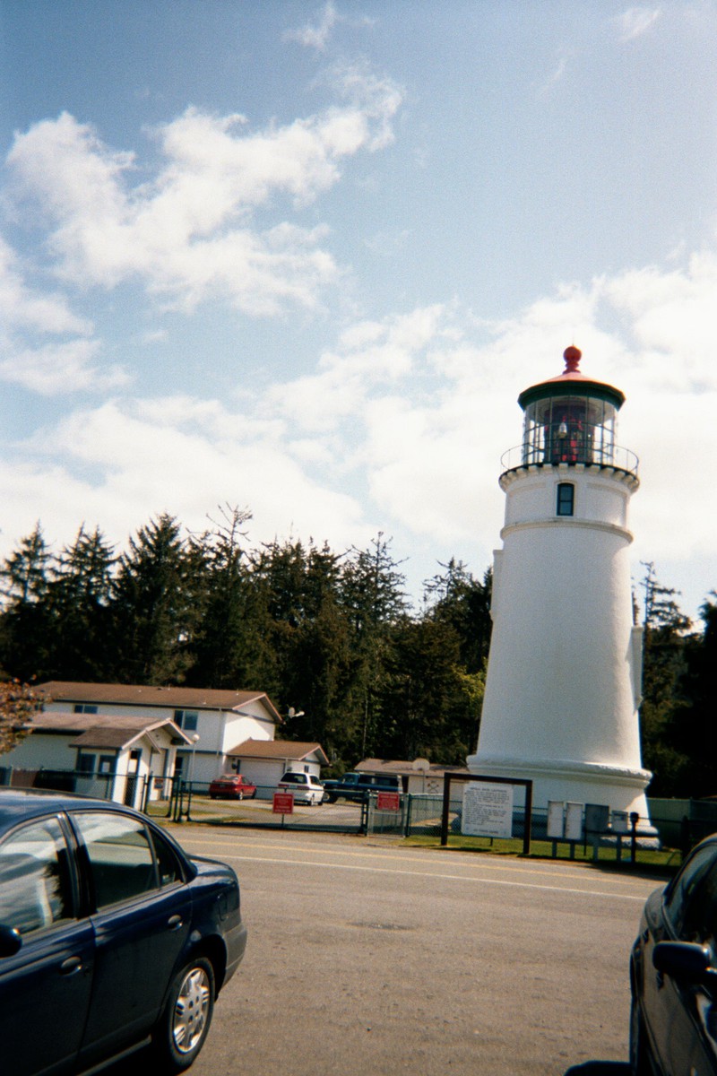A squat white lighthouse next to a parking lot