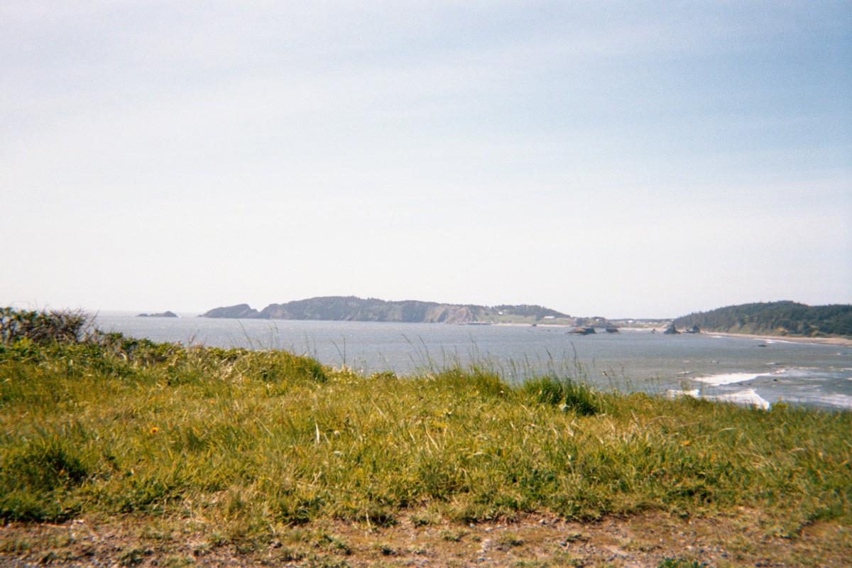 View from a done across a broad bay toward a grassy headland. Weather very sunny, windy