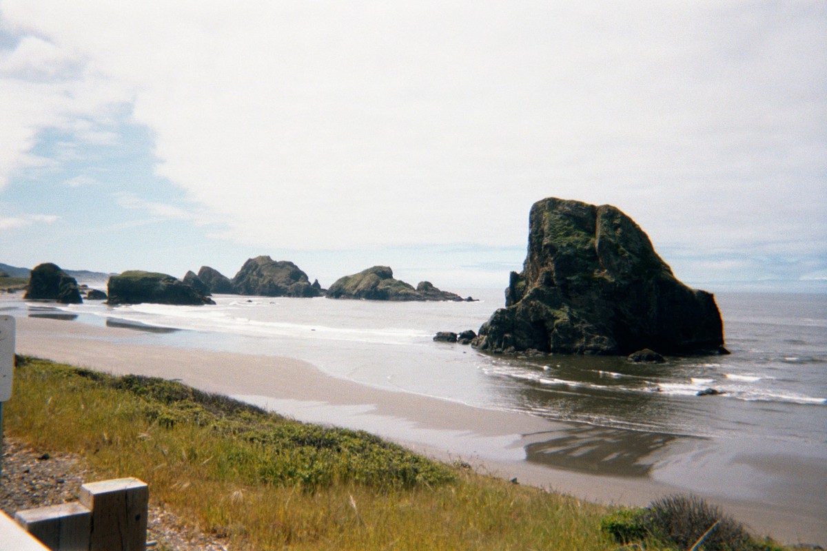 Broad empty sandy beach with tall rocks & seastacks, taken from a highway immediately along the shore. Weather windy & sunny