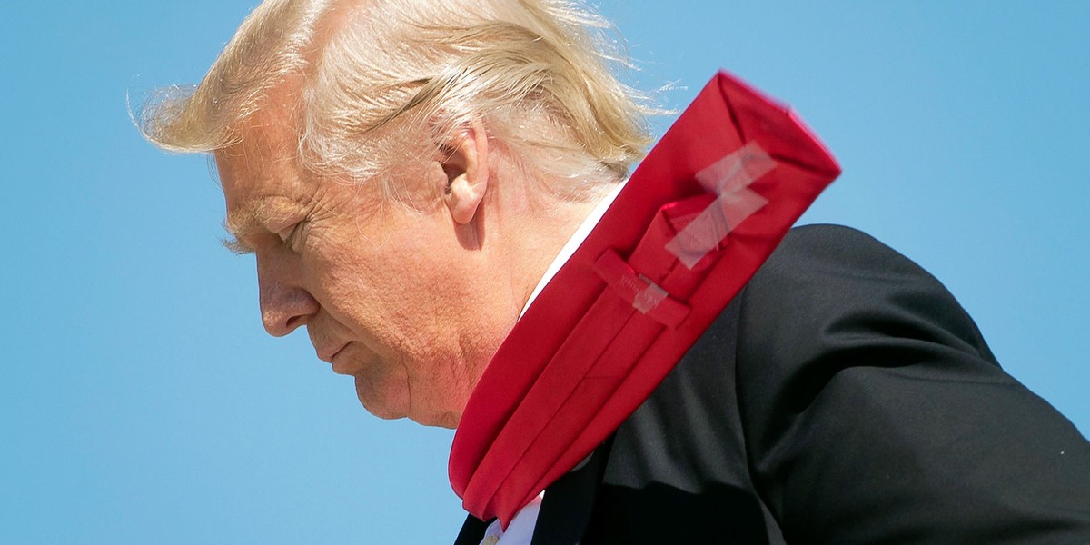 Donald Trump in a strong wind with his tie blowing over his shoulder. The scotch tape holding the skinny end of the tie to the fat end is visible