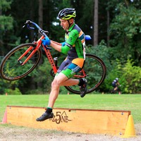 Man in cyclocross skinsuit jumping a barrier with a bicycle at a race