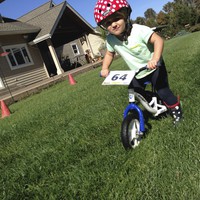 Preschooler on a scoot bike with a serious face on a lawn at a kiddie kross race