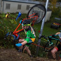 Middle aged man in Team Oregon skinsuit, shouldering a cyclocross bike, climbing almost as if on a ladder up a very steep runup through blackberries. Taken at Edgefield resort, Troutdale Oregon
