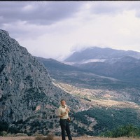Scan of a Kodachrome slide, landscape, 1969. A young man in the near foreground in front of a long valley in Greece, with broken sun and weather clouds sweeping across it