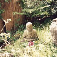 Closeup of a small stone buddha with a flower in front of it, taken at the San Francisco Japanese Gardens, 1992