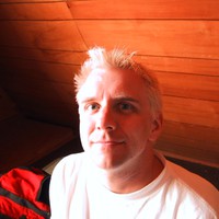 Moderate closeup, indoors in a rustic cabin, a young man with short bleached white hair making a cryptic smile
